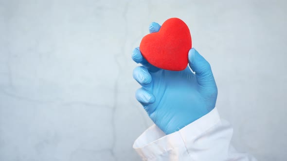 Man Hand in Protective Gloves Holding Red Heart on Blue alt