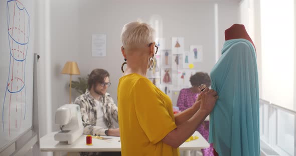 Mature Woman Fashion Designer Straightening Fabrics on Tailored Mannequin alt