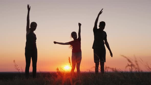 Young Family with a Child Doing Exercises in a Beautiful Place at Sunset alt