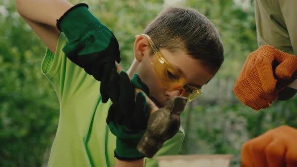 Boy in Goggles Hammers Nail Under Control of Carpenter