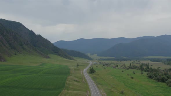 Asphalt road between green field and mountains in Altai