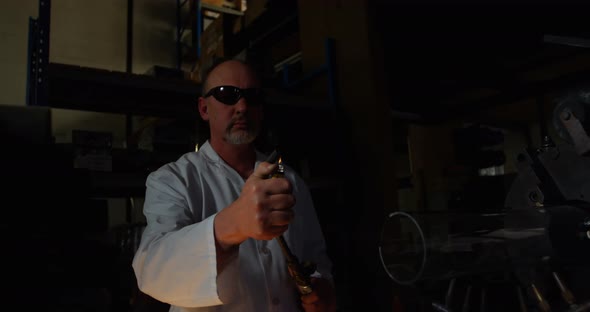 Front view of mature male worker lighting glass blowing torch in glass factory 4k alt