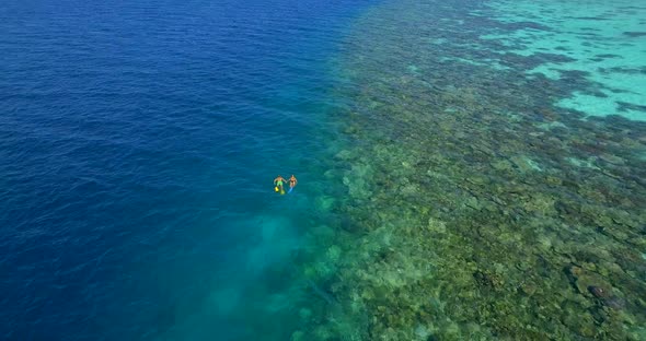 Aerial drone view of a man and woman couple snorkeling over a coral reef of a tropical island alt