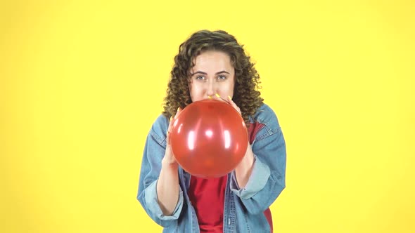 Curly Girl Inflates a Red Ball Then Blows It Off on Yellow Background, Slow Motion. alt