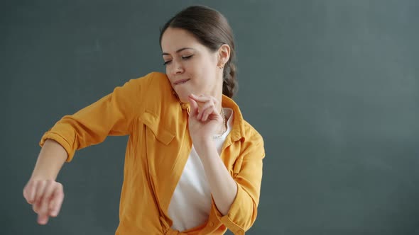 Slow Motion of Playful Young Lady in Casual Clothing Dancing Snapping Fingers on Gray Background alt