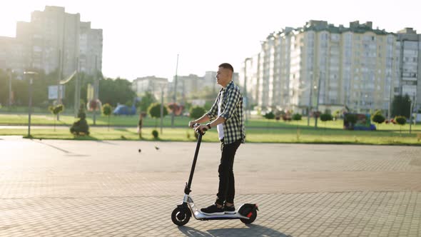 Hipster Man Commuting to Work Through City on Electric Scooter Ecology and Urban Lifestyle