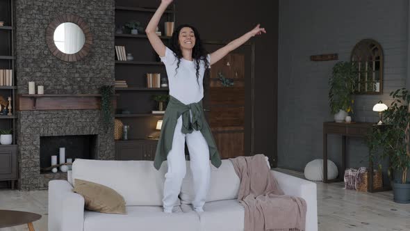 Young Funny Happy Carefree Cheerful Woman Housewife Actively Moves Dynamically Dances on Sofa in alt