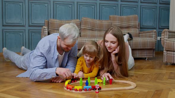 Family of Mother Father with Daughter Child Girl Riding Toy Train on Wooden Railway at Home Room alt