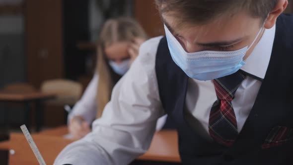 A Student in a Medical Mask Writes in the Classroom at the Desk