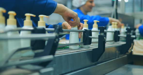 Hands of Women Who Spin the Dispenser on the Plastic Bottles on the Conveyor Belt of the Chemical alt
