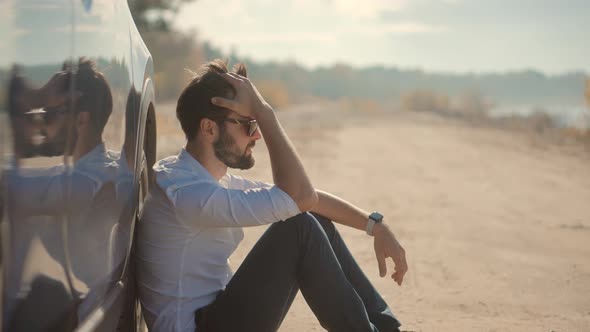 Sad Disappointed Man Sitting On Broken Car. Sad Exhausted Businessman. alt
