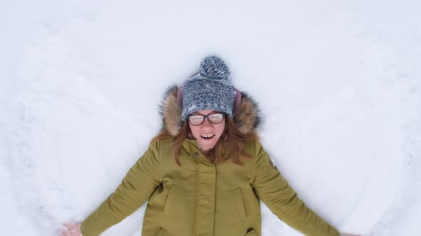 Young Woman Making Snow Angel and Laughing