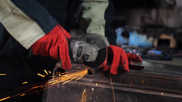 Closeup of a Male Master in Red Work Gloves with a Grinding Machine for Cutting Cuts Off a Profile