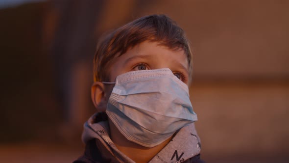 Kid in face protective mask is scarred of emergency siren with red light outdoors.  alt