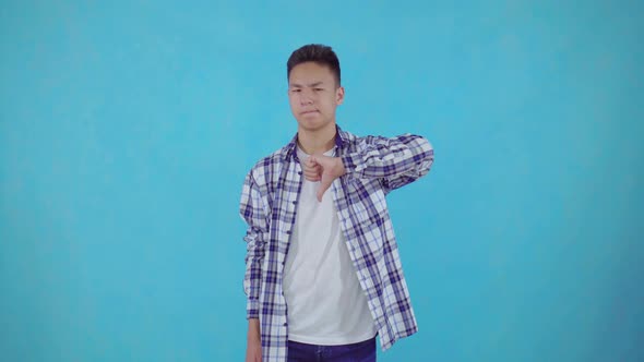 Dissatisfied Young Asian Man Shows Sign of Dislike on Blue Background alt