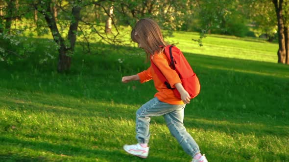 Camera Movement on Little Child Girl with School Backpack Runs and Laughs on Lawn in Summer Park