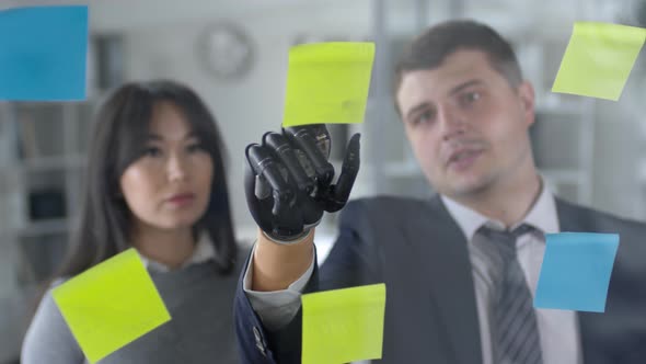 Man with Prosthetic Hand Discussing Plans on Sticky Notes with Female Coworker alt