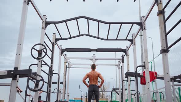 Athletic Man Pumps Up Muscles Doing PullUps Open Sports Ground with Bare Torso alt