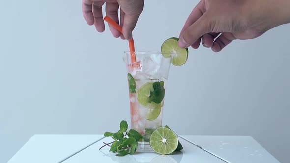 Man Takes Out Straw and Lime Slice From Glass on White Table alt