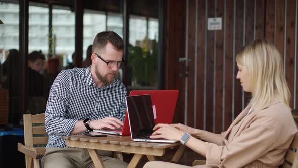 Young Lady and Handsome Guy Are Sitting at Table in Open Cafe Work with Laptops alt