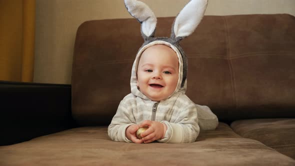 Cute Little Baby with Bunny Ears Smiling Holding Easter Egg alt