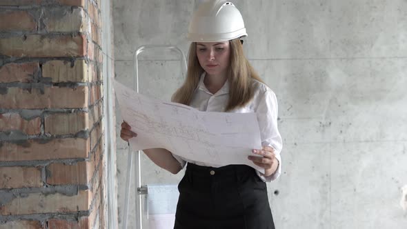 The girl engineer builder is checking the drawings at the apartment of the projected house. alt