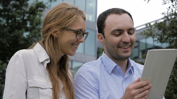 Smiling man and woman using tablet pc outdoors. alt