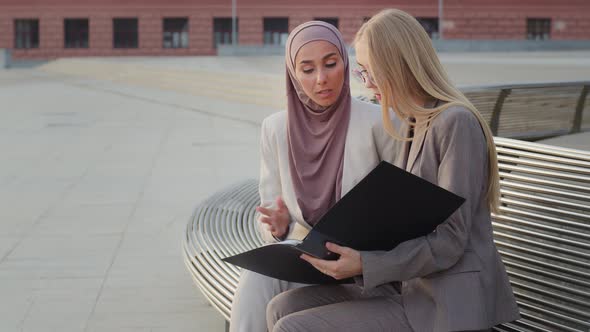 Serious Businesswomen in Business Suits Holding Folder with Documents Discussing Report alt