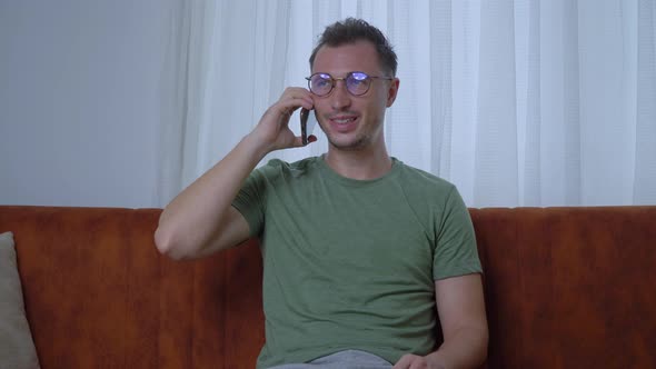 A Man with Glasses Communicates on the Phone Sitting on the Couch of the House Closeup