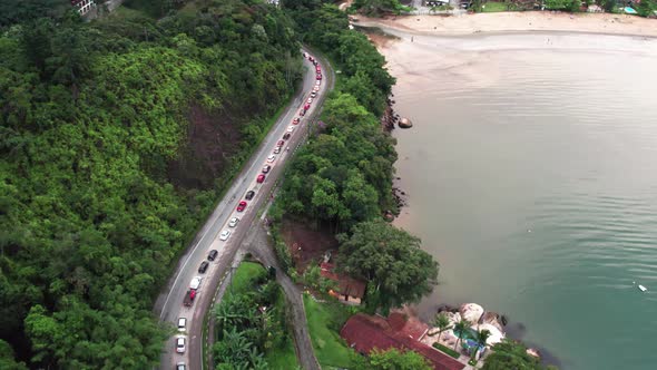Traffic jam at end of day in coastal road, descent to Ubatuba beach, Brazil. Aerial forward alt