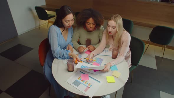 Busy Multiracial Female Coworkers Discussing Financial Documents at Cafe alt