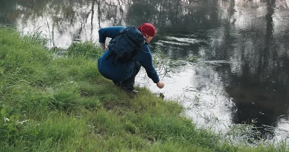Hiker with a Backpack Drinks Water From an Unfamiliar River