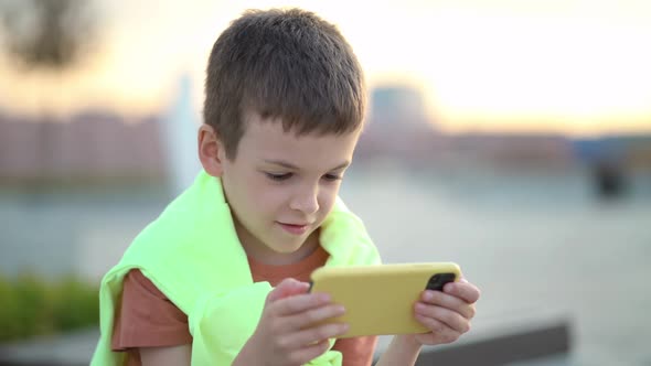 Boy Watching Cartoons on His Phone While Sitting on a Bench in the Park alt