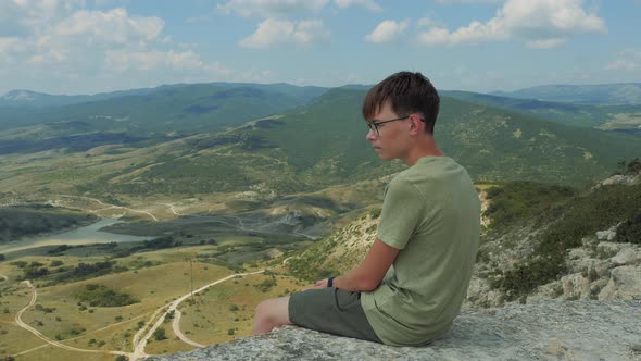 Young Guy Tourist in Glasses Sits on the Edge of Mountain, Feodosia Highlands, Crimea