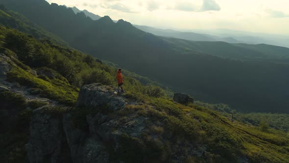 Man Standing At The Peak Of Rock Mountain and Looking at the Green Valley Below alt
