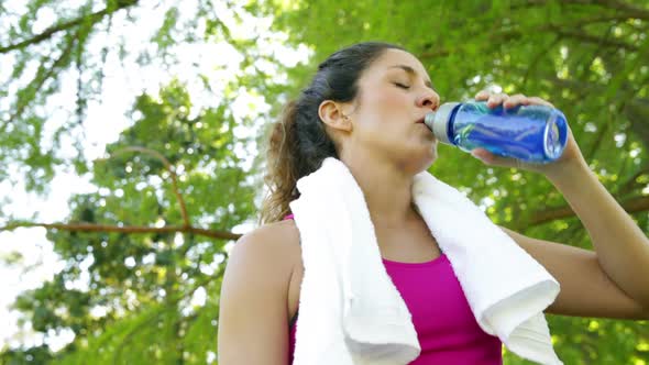 Woman wiping her brow and drinking water after workout in the park alt