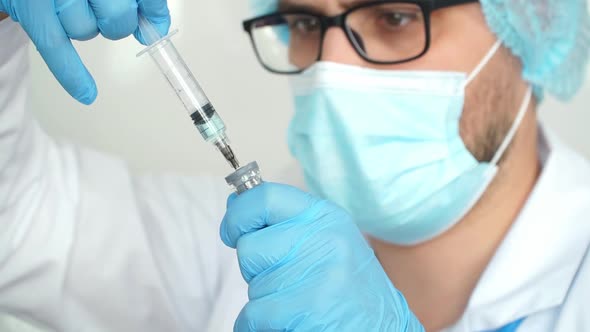 Close Up of Male Doctor in Protective Mask Fills Syringe with Vaccine for Covid19