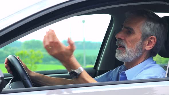 Senior Man Sits in the Car and Complains on Traffic Situation - Closeup Shot From Side - Countryside alt