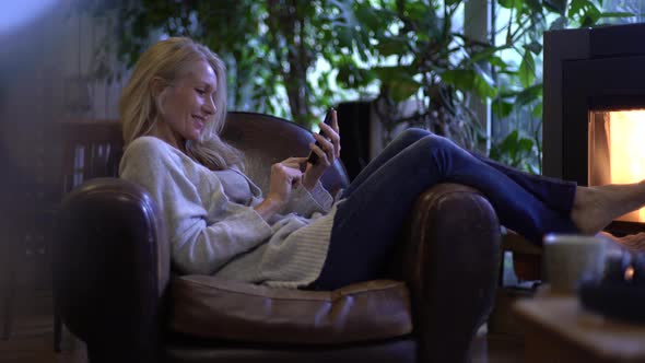 Mature woman texting on her smart phone at home alt