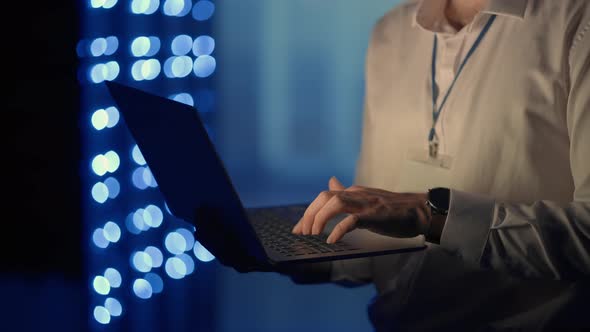 Male Network Engineer Doing a System Check Standing in the Server Room with His Laptop alt