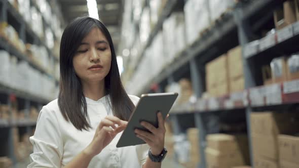 Female worker checking products with tablet in warehouse.