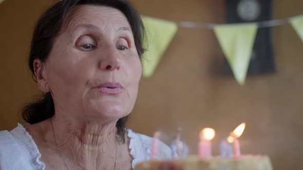 Happy Birthday, Elderly Woman Enjoys Holiday and Blows Out Burning Candles on Sweet Birthday Cake alt
