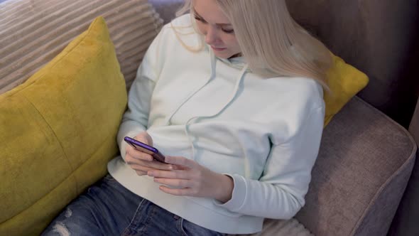 Young female user using mobile phone while sitting on sofa at home. alt