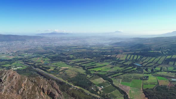 Aerial - Farms looking like stitched together patches, flying backwards revealing edge of mountain, alt