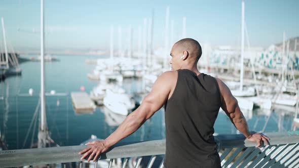 Bald serious sportsman wearing black T-shirt looking at the sea outdoors alt