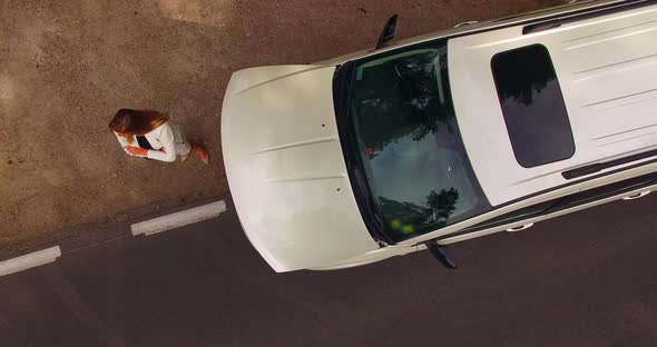 4k aerial shot of a stranded young woman looking under the hood of her broken down car. alt