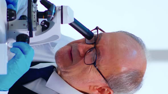 Vertical Video Senior Lab Technician Examining Samples and Liquid Using Microscope alt