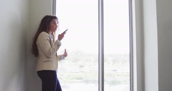 Biracial businesswoman smiling and talking on smartphone in modern interiors alt