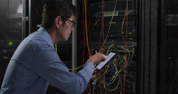 Asian male it technician using tablet checking computer server alt