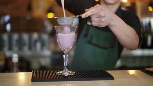 Bartender Pouring Pink Cocktail in Crystal Glass Holding a Strainer alt